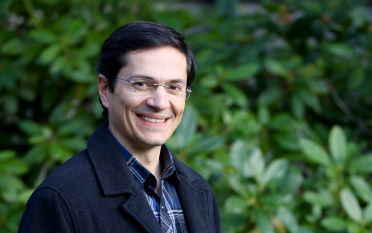Carlos Brito, VP of Engineering - Dark haired man in a black jacket on a green leafy background