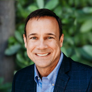 Smiling man in a blue suit on a green background - Jeff Ressler